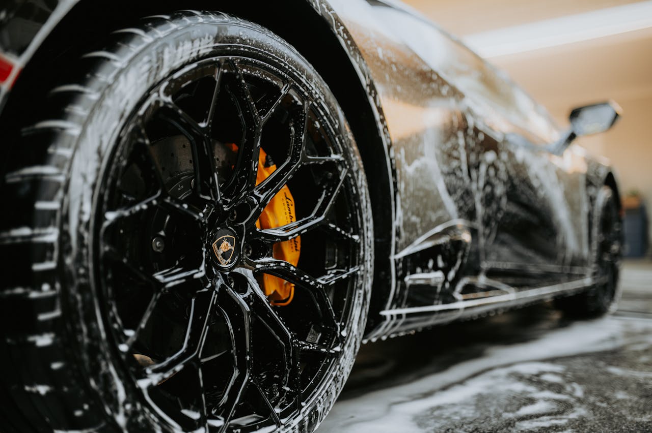 about-01 Detailed close-up of a luxury car wheel covered in soap suds during a professional car wash.