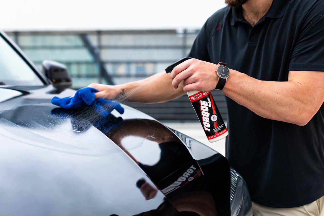 who-we-are-03 A man cleaning a black car hood with a spray and microfiber cloth.